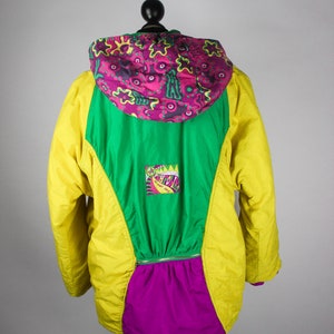 May include: A yellow, green and purple jacket with a colourful patterned hood. The jacket has a zip closure and a logo patch on the front.