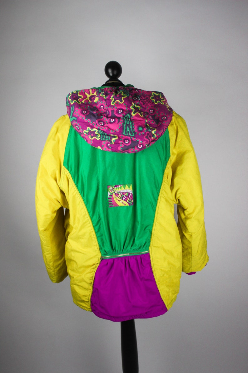 May include: A yellow, green and purple jacket with a colourful patterned hood. The jacket has a zip closure and a logo patch on the front.