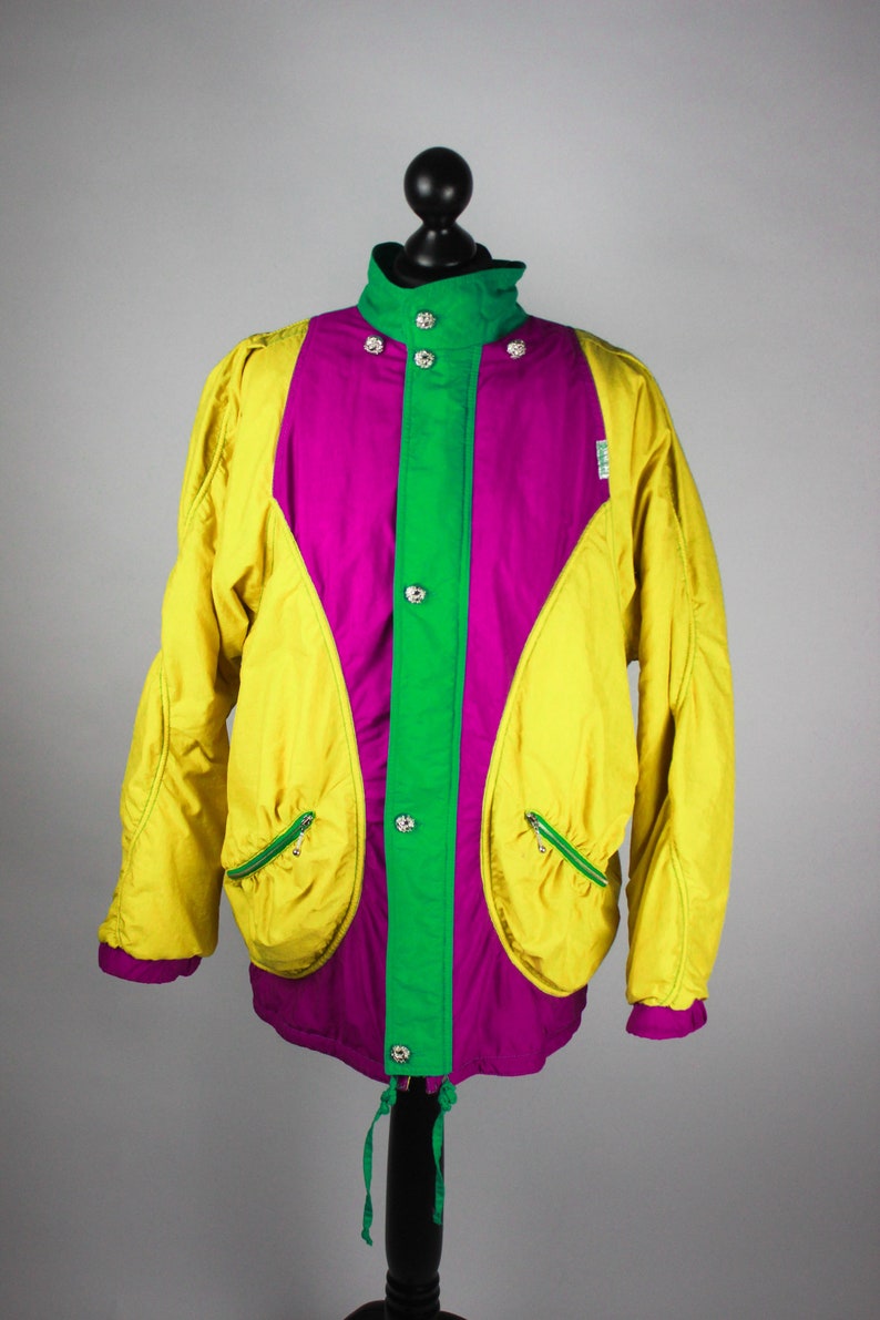 May include: A yellow, green and purple jacket with a snap closure and two zipped pockets. The jacket has a drawstring at the bottom.