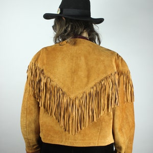 May include: A brown suede jacket with fringe detailing. The jacket has a V-shaped yoke and a cropped length.