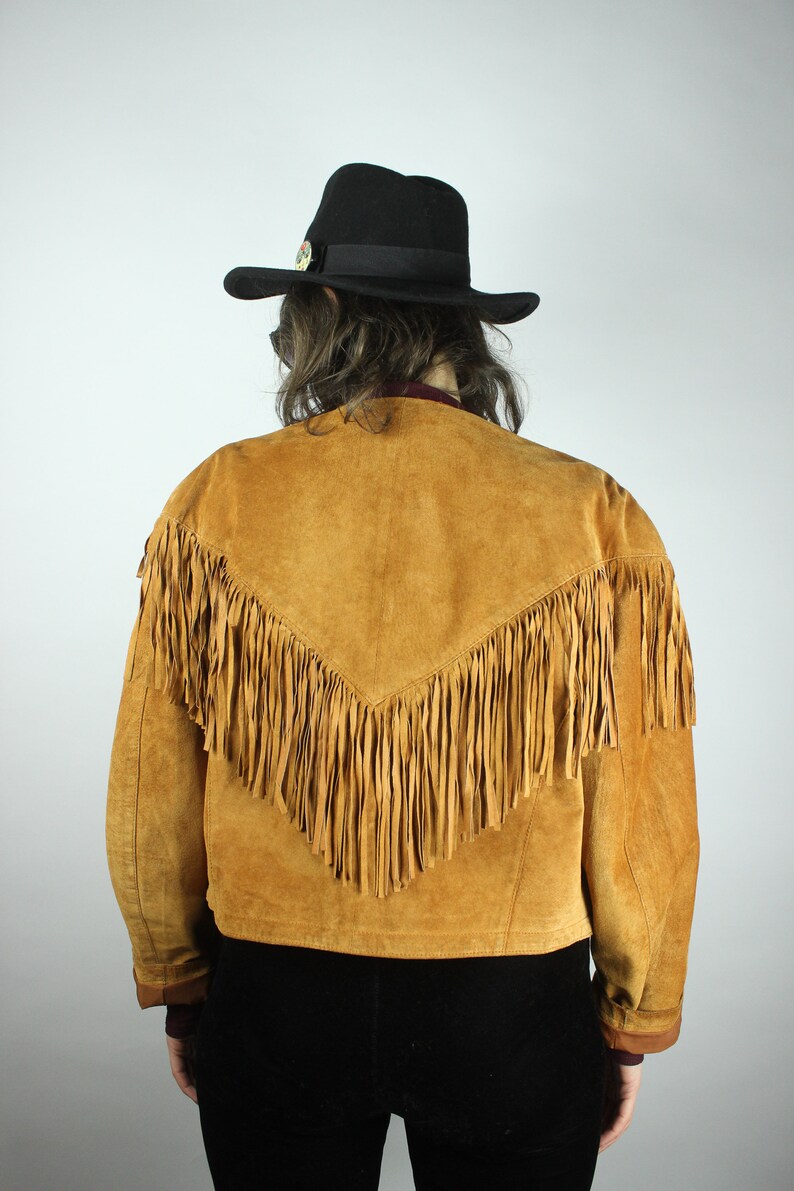 May include: A brown suede jacket with fringe detailing. The jacket has a V-shaped yoke and a cropped length.