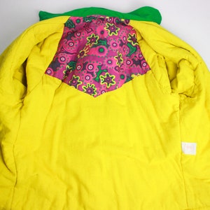 May include: A green and yellow jacket with a pink and green floral lining. The jacket has a zip closure and a small tag on the inside.