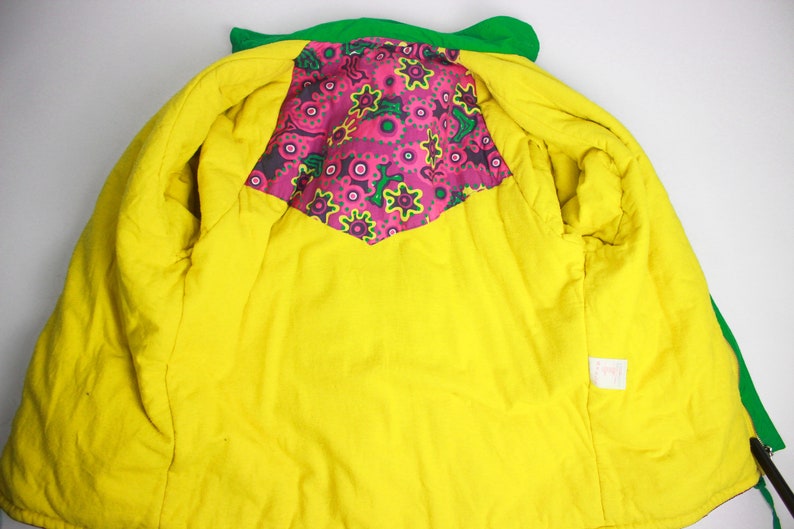 May include: A green and yellow jacket with a pink and green floral lining. The jacket has a zip closure and a small tag on the inside.