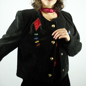 May include: A black suede jacket with a red diamond-shaped patch and colourful embroidery. The jacket has a button-up front and a collar.