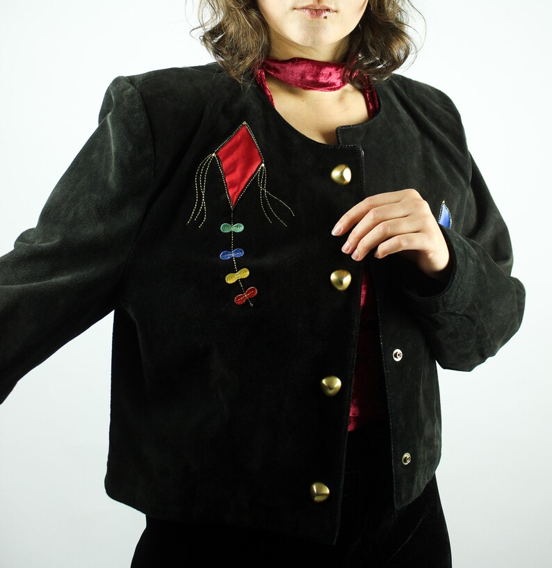 May include: A black suede jacket with a red diamond-shaped patch and colourful embroidery. The jacket has a button-up front and a collar.