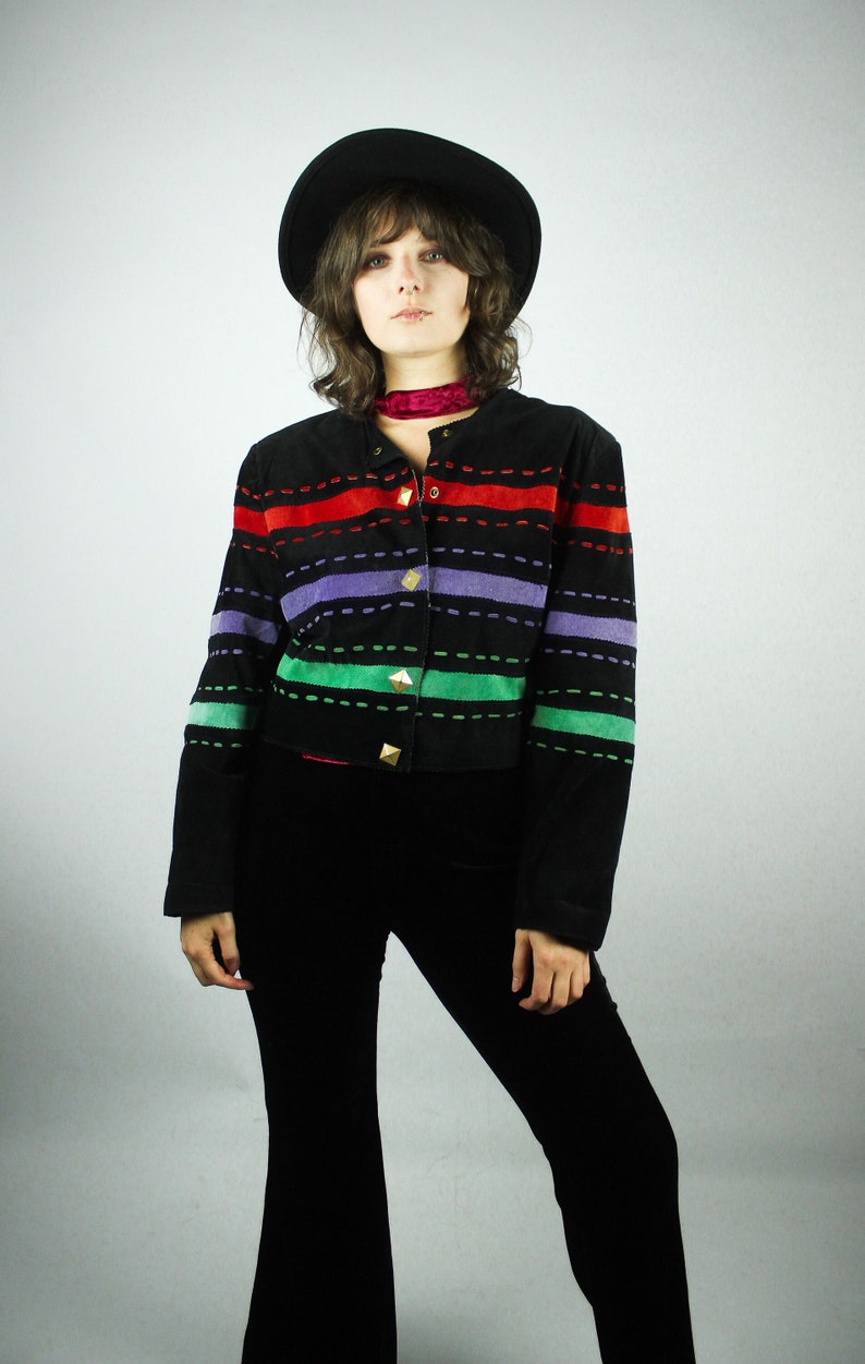 May include: A black suede jacket with colorful striped detailing and gold buttons. The jacket has a cropped fit and long sleeves.