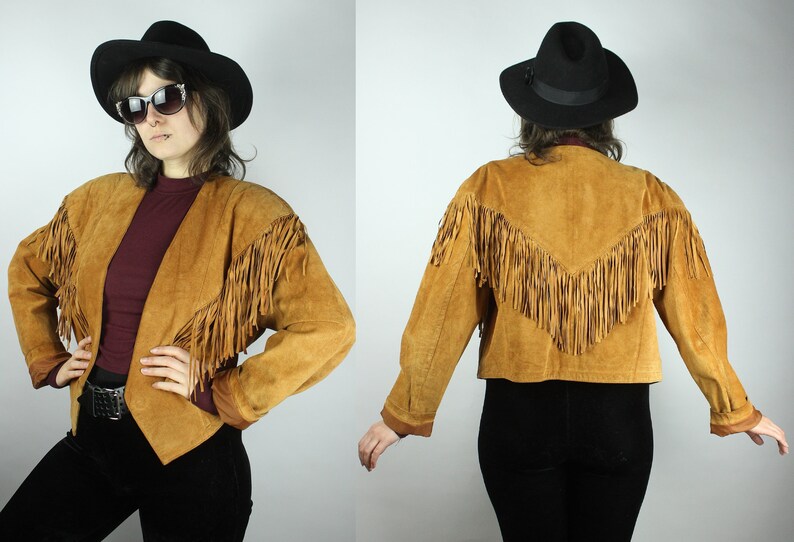 May include: A brown suede jacket with fringe detailing. The jacket has a pointed collar and long sleeves. The jacket is cropped and has a fitted silhouette.
