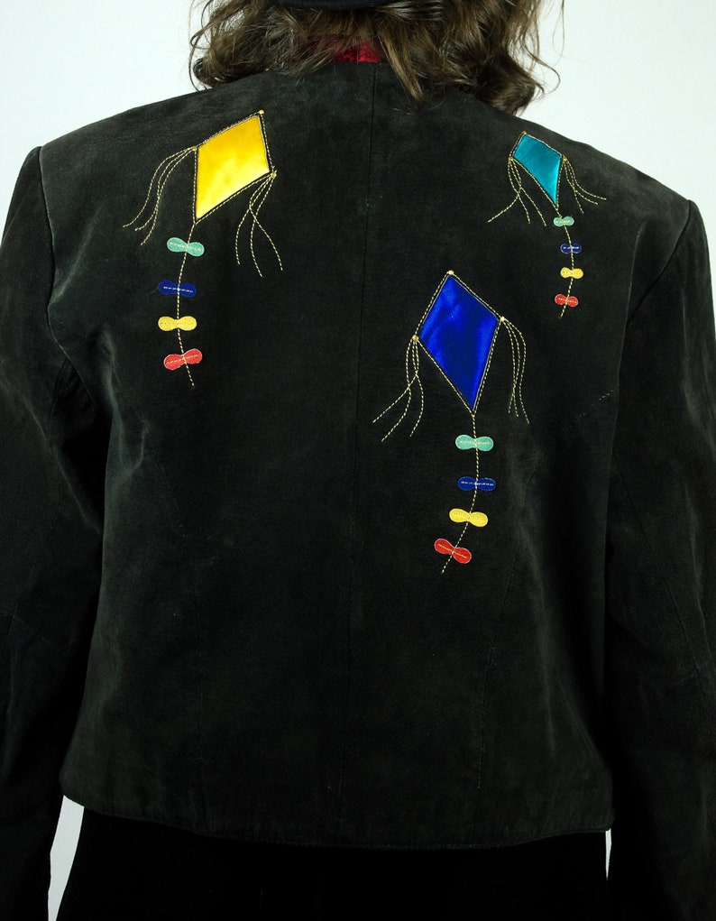 May include: A black suede jacket with three colourful embroidered kites on the back. The kites are yellow, blue and green with red and yellow string details.