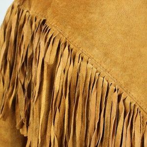 May include: A brown suede jacket with fringe detail. The fringe is made of the same material as the jacket and is sewn along the seams.