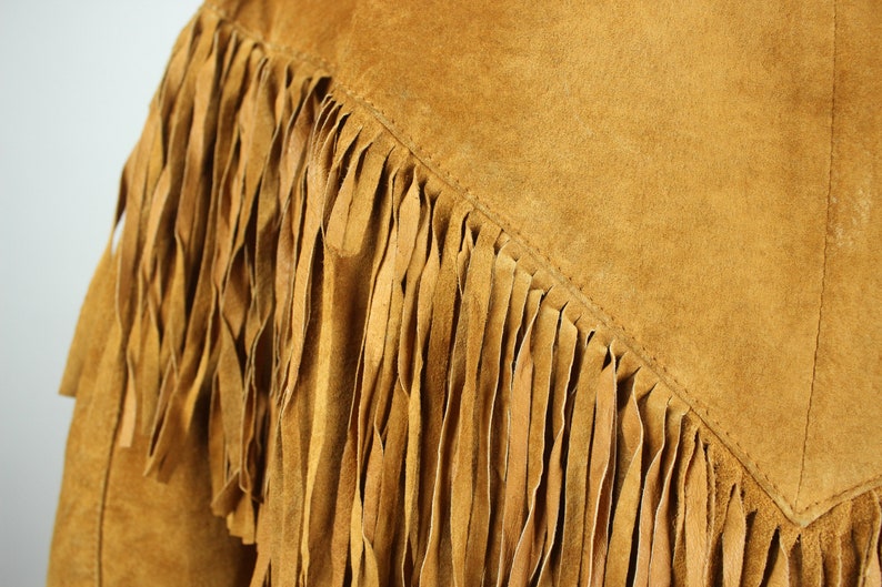 May include: A brown suede jacket with fringe detail. The fringe is made of the same material as the jacket and is sewn along the seams.