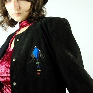 May include: A black suede jacket with a colourful kite design on the front. The jacket has a red velvet collar and a button closure.