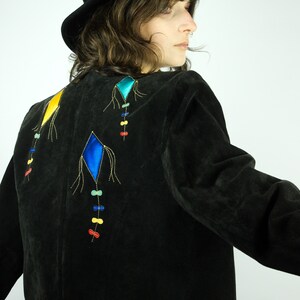 May include: A black suede jacket with colourful embroidered kite designs on the back. The jacket has a cropped length and long sleeves.