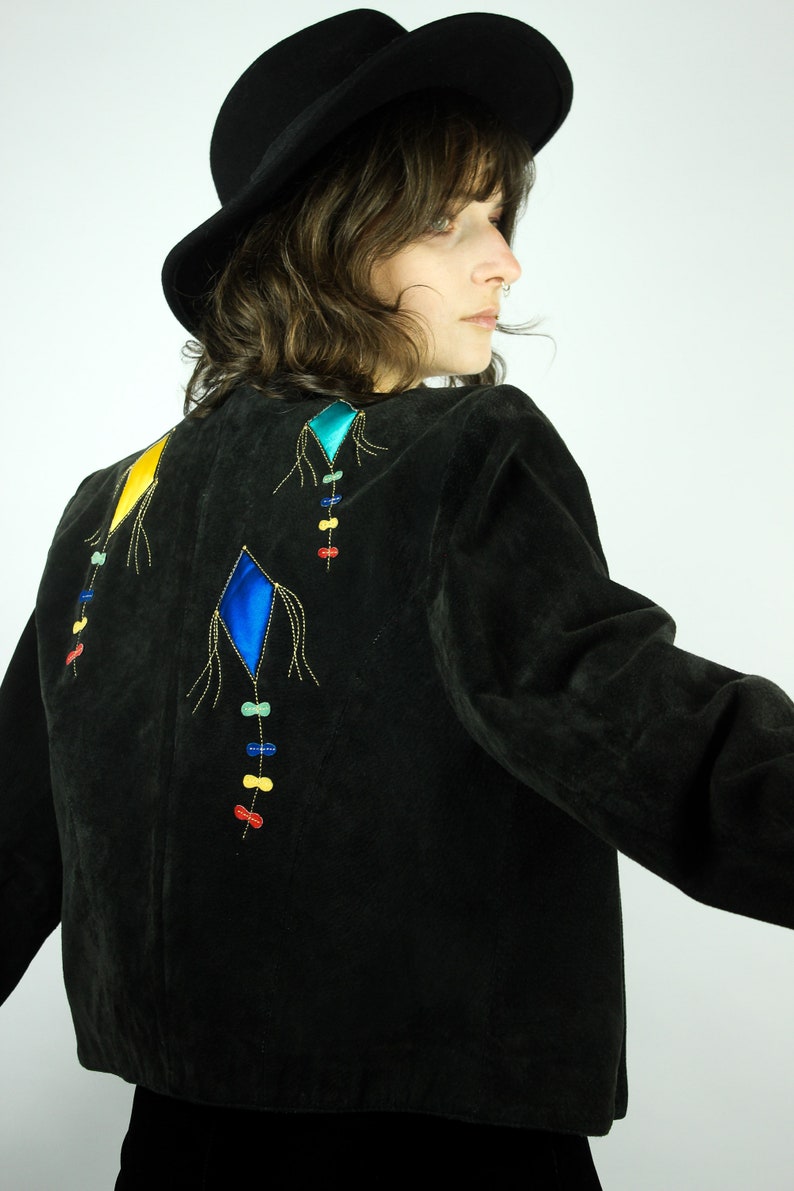 May include: A black suede jacket with colourful embroidered kite designs on the back. The jacket has a cropped length and long sleeves.