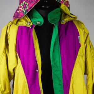 May include: A yellow, green and purple ski jacket with a colourful patterned hood. The jacket has a zip closure and multiple pockets.