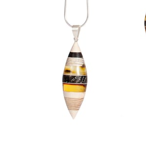 以下が含まれることがあります： 銀色のチェーンネックレスに、琥珀、骨、木で作られた涙型のペンダントがついたもの。ペンダントは、琥珀、黒、白のストライプが層状になったデザインです。