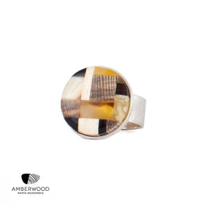 Peut inclure: Une bague en argent avec une pierre ronde multicolore. La pierre est faite d'ambre, de bois et d'autres matériaux. La bague est un bijou unique et élégant.