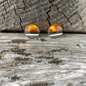 May include: A pair of round amber earrings with a black and white stripe design. The earrings are set in silver.