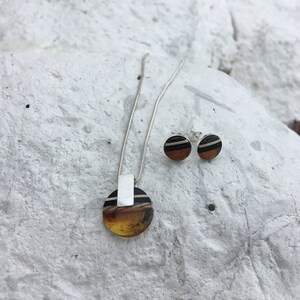 May include: A silver necklace with a round amber pendant and matching earrings. The pendant and earrings have black and white stripes.