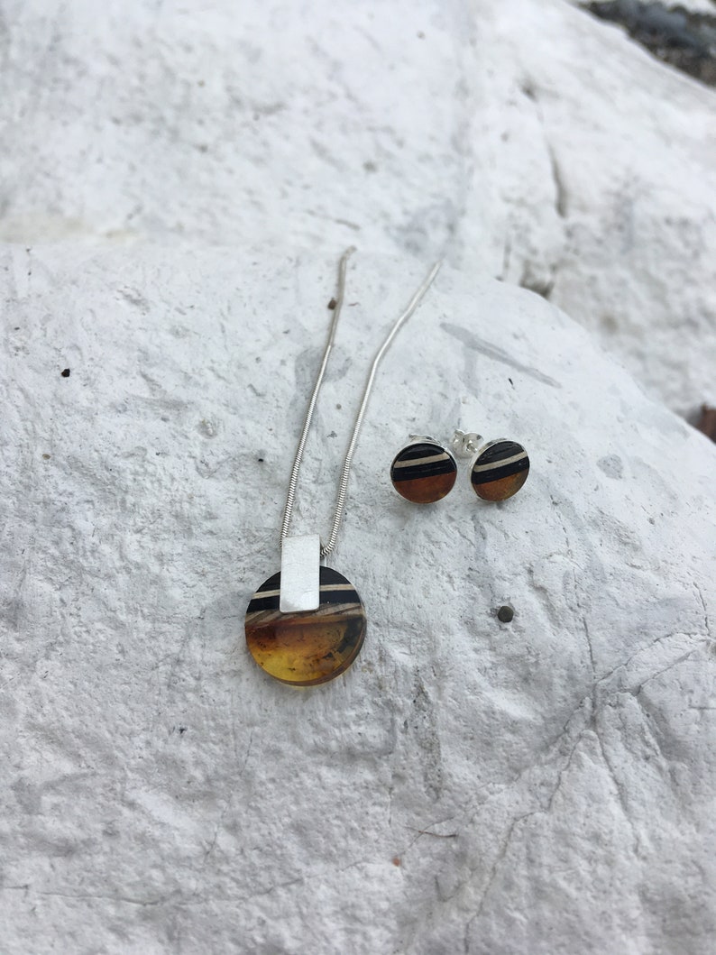 May include: A silver necklace with a round amber pendant and matching earrings. The pendant and earrings have black and white stripes.