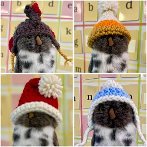 May include: Four stuffed owls wearing different knitted hats. The hats are a brown and white turkey, a yellow and orange striped hat, a red and white Santa hat, and a blue and white striped hat.