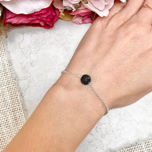 May include: A silver chain bracelet with a single black lava rock bead.