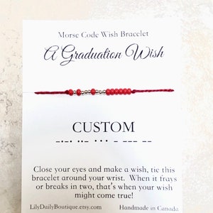 Puede incluir: Pulsera de deseos en código Morse con cuentas rojas y doradas y una tarjeta blanca que dice "Morse Code Wish Bracelet A Graduation Wish CUSTOM" y "Cierra los ojos y pide un deseo, ata esta pulsera alrededor de tu muñeca. Cuando se deshilache o se rompa en dos, es cuando tu deseo podría hacerse realidad! LilyDailyBoutique.etsy.com Hecho a mano en Canadá"
