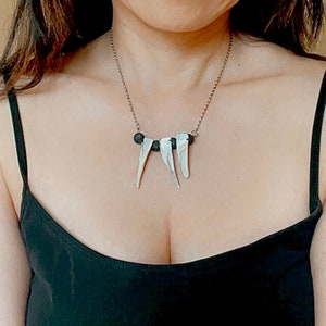 Puede incluir: Un collar de cadena de plata con tres colgantes de concha blanca y tres cuentas negras.