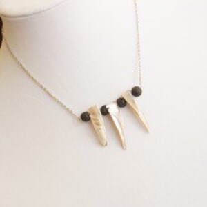 May include: A silver necklace with three gold-toned spikes and black beads.