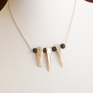 May include: A silver chain necklace with three white shell pendants and black lava rock beads.