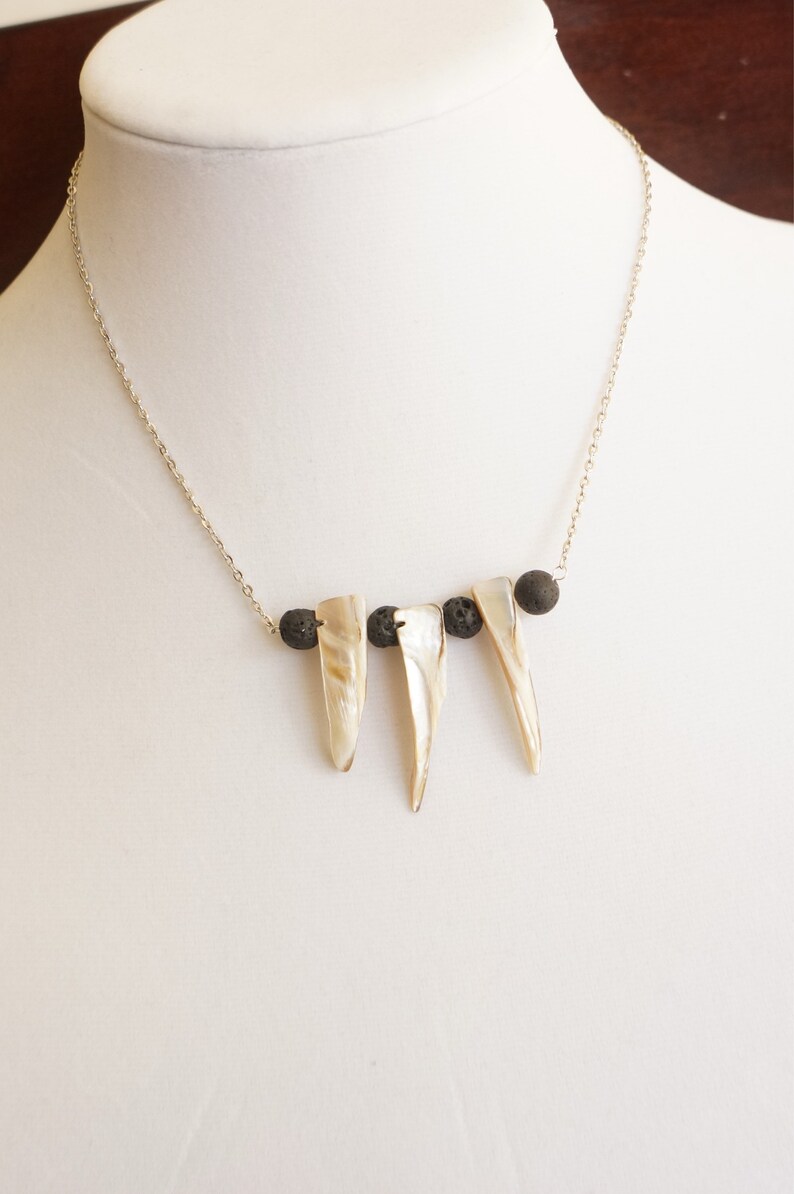 May include: A silver chain necklace with three white shell pendants and black lava rock beads.