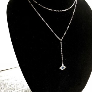 May include: A silver chain necklace with a silver evil eye pendant. The pendant has a blue stone in the center.