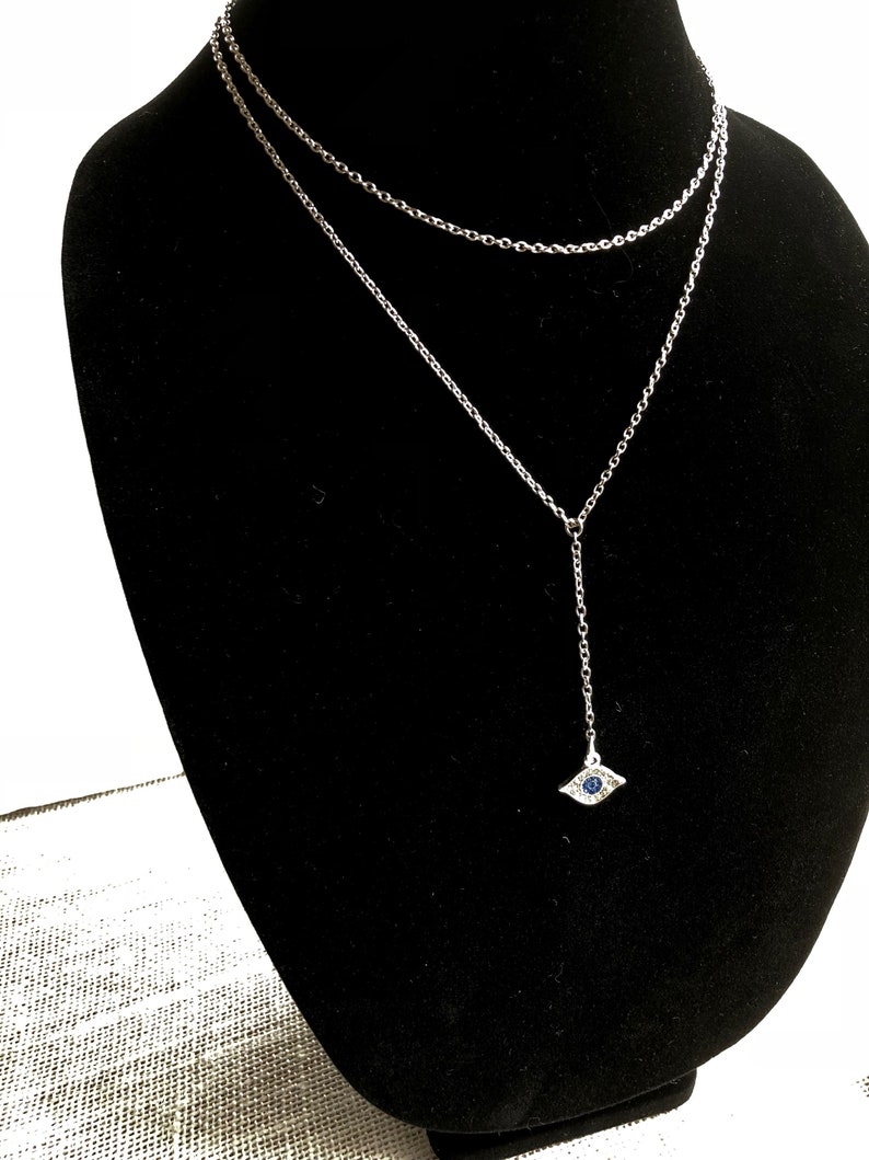 May include: A silver chain necklace with a silver evil eye pendant. The pendant has a blue stone in the center.