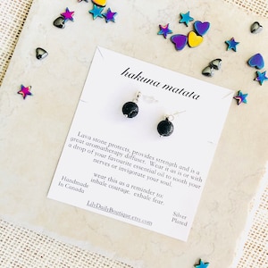 Op de afbeelding: Een paar zwarte lavastenen oorbellen met zilveren haakjes. De oorbellen liggen op een witte kaart met de tekst "hakuna matata" en een beschrijving van de oorbellen. De tekst "Zilver Gecoat" staat ook op de kaart.