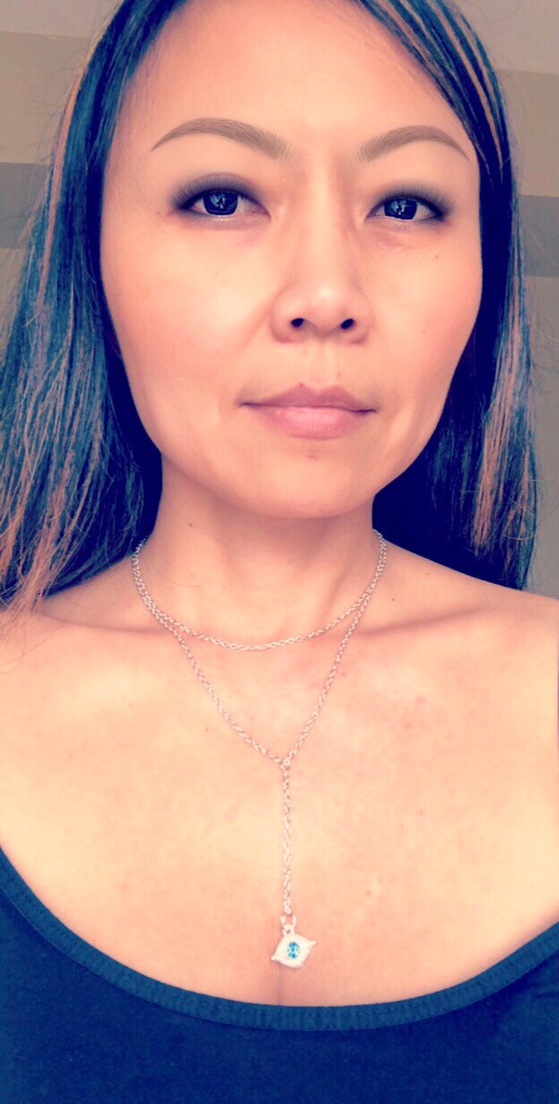 May include: A woman wearing a black tank top with a silver chain necklace with a blue eye charm pendant.