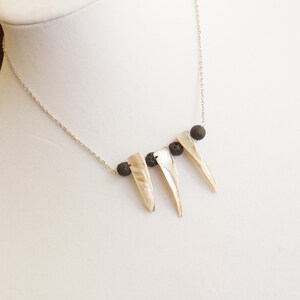 May include: A silver chain necklace with three white shell pendants and three black lava rock beads.