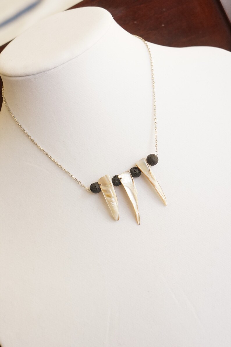 May include: A silver chain necklace with three white shell pendants and three black lava rock beads.