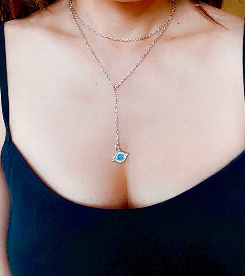 May include: A silver chain necklace with a blue evil eye pendant. The necklace is layered with a shorter chain.