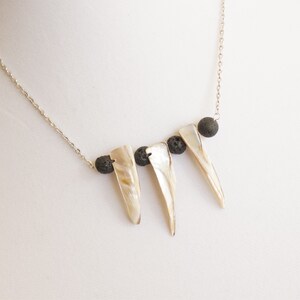 May include: A silver chain necklace with three white shell pendants and three black lava rock beads.