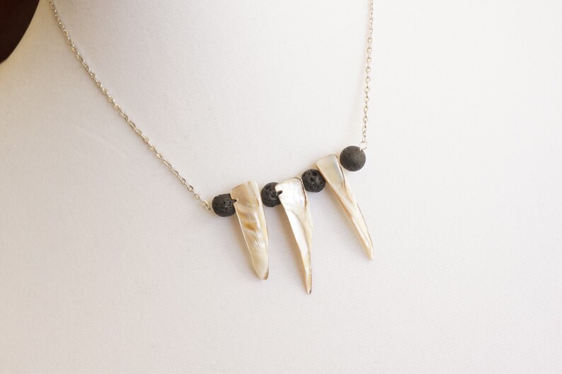 May include: A silver chain necklace with three white shell pendants and three black lava rock beads.