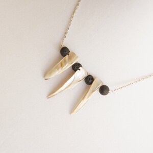 May include: A gold chain necklace with three white shell pendants and black lava rock beads.