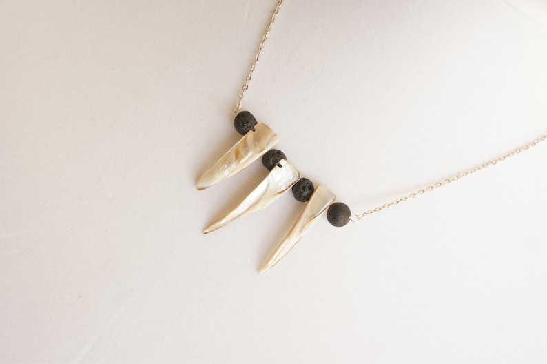 May include: A gold chain necklace with three white shell pendants and black lava rock beads.