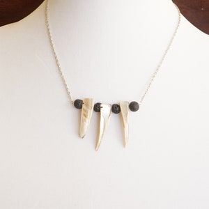 May include: A silver chain necklace with three white shell pendants and three black lava rock beads.