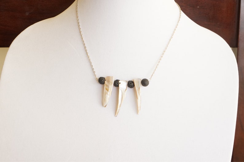 May include: A silver chain necklace with three white shell pendants and three black lava rock beads.