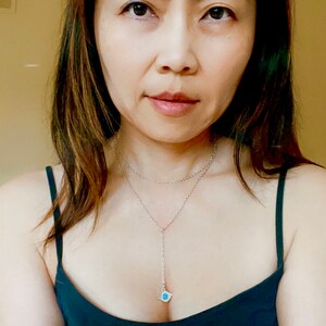May include: A woman with long brown hair wearing a dark blue sleeveless top with a silver necklace with a blue pendant.
