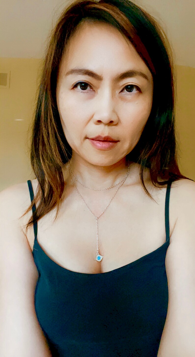 May include: A woman with long brown hair wearing a dark blue sleeveless top with a silver necklace with a blue pendant.