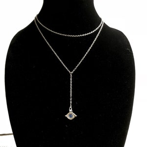May include: A silver chain necklace with a silver evil eye pendant. The pendant has a blue stone in the center.