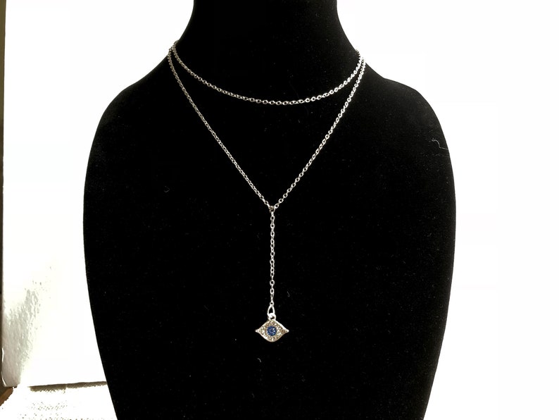 May include: A silver chain necklace with a silver evil eye pendant. The pendant has a blue stone in the center.