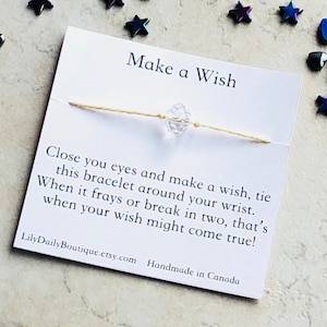 Op de afbeelding: Witte kaart met de tekst "Make a Wish" en instructies over hoe je een wens kunt doen met een armband van touw. De armband heeft een heldere kristallen kraal. De kaart bevat ook de tekst "LilyDailyBoutique.etsy.com Handgemaakt in Canada".
