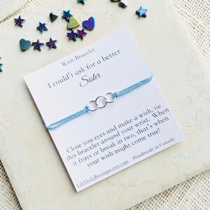 May include: A light blue wish bracelet with three silver rings. The card reads "Wish Bracelet I couldn't ask for a better Sister Close you eyes and make a wish, tie this bracelet around your wrist. When it frays or break in two, that's when your wish might come true! LilyDailyBoutique.etsy.com Handmade in Canada"