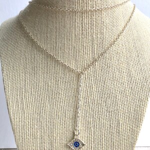 May include: A silver chain necklace with a blue evil eye charm. The charm is set with clear rhinestones and has a blue center.